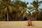 A young adult man sits on the sand of Karon Beach in Thailand on a background of coconut palm trees