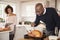 Young adult mixed race couple preparing Christmas dinner together at home, man basting roast turkey in the foreground, front view,