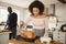 Young adult mixed race couple preparing Christmas dinner together at home, woman basting roast turkey in the foreground, front vie