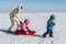 Young adult mother wear warm jacket enjoy have fun sledging two cute little sibling kids boy girl at frozen white snow