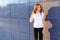 Young adult pretty female girl student smiling, straightens hair, posing for camera and stands near business cente.