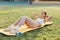 Young adult slim woman in sportswear lies on mat at stadium and practices crunching on the abdominal muscles, training outdoor.