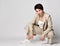 Young adult woman in beige business casual pantsuit and sneakers sits squatted, smiling. Stylish business female wear