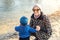 Young adult woman with cute toddler boy having funfeeding birds near lake or pond at city park on bright atumn day. Mother with