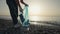 Young adult woman picking up some abandoned plastic bottles on the beach. Women collecting garbage on the beach.