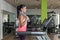 Young adult woman wearing sportswear walking on a treadmill with a towel around her neck looking to the panel of machine