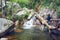 Young adventure girl on the river with waterfall and a tree trunk fallen into the water