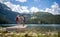 Young adventurous couple holding hands and excited on wooden jetty by lake. Pointing to distance. Love, adventure, hiking, nature