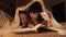 Young affectionate mother and child daughter reading book using a flashlight before going to bed