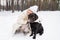 Young affectionate smiling woman embracing black retriever sitting on snow