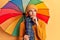 Young african amercian man holding colorful umbrella serious face thinking about question with hand on chin, thoughtful about