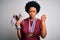 Young African American afro athlete woman with curly hair wearing medals holding trophy annoyed and frustrated shouting with