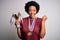 Young African American afro athlete woman with curly hair wearing medals holding trophy screaming proud and celebrating victory