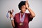 Young African American afro athlete woman with curly hair wearing medals holding trophy stressed with hand on head, shocked with