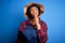 Young African American afro farmer woman with curly hair wearing apron and hat with hand on chin thinking about question, pensive