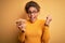 Young african american afro girl holding bowl with healthy peanuts over yellow background screaming proud and celebrating victory