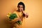 Young african american afro romantic man with dreadlocks holding bouquet of yellow tulips Pointing with finger up and angry