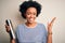 Young African American afro tourist woman with curly hair holding thermo with water very happy and excited, winner expression