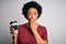 Young African American afro woman with curly hair drinking cup of coffee cover mouth with hand shocked with shame for mistake,