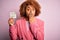 Young African American afro woman with curly hair holding papaer with tax day message cover mouth with hand shocked with shame for