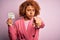 Young African American afro woman with curly hair holding papaer with tax day message pointing with finger to the camera and to