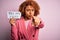 Young African American afro woman with curly hair holding papaer with you are fired message pointing with finger to the camera and