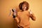 Young African American afro woman with curly hair holding winner champion trophy happy with big smile doing ok sign, thumb up with