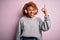 Young African American afro woman with curly hair listening to music using pink headphones pointing finger up with successful idea