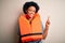 Young African American afro woman with curly hair wearing orange protection lifejacket with a big smile on face, pointing with