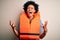 Young African American afro woman with curly hair wearing orange protection lifejacket crazy and mad shouting and yelling with