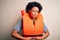 Young African American afro woman with curly hair wearing orange protection lifejacket with hand on stomach because nausea,