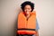 Young African American afro woman with curly hair wearing orange protection lifejacket with a happy and cool smile on face