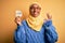 Young African American afro woman wearing muslim hijab holding love reminder paper message doing ok sign with fingers, excellent