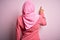 Young African American afro woman wearing muslim hijab over isolated pink background Posing backwards pointing ahead with finger