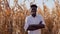 Young african american agronomist farmer standing in the middle of a corn field and smiling