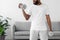 Young african american bearded man in white sportswear raises dumbbells in living room interior, cropped
