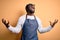 Young african american cooker man wearing apron and over isolated yellow background crazy and mad shouting and yelling with