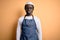 Young african american cooker man wearing apron and over isolated yellow background with serious expression on face