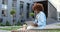 Young African American curly beautiful woman sitting on bench, talking via webcam on laptop computer and laughing