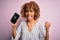 Young african american curly woman holding broken smartphone showing craked screen screaming proud and celebrating victory and