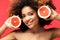 Young African American female with perfect skin holding sliced grapefruit next to face and looking at camera