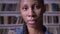 Young african american female student looking into camera and standing in library, serious and concerned