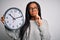Young african american girl holding big minute clock over  background serious face thinking about question, very confused