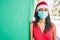 Young african american girl wearing christmas hat and medical mask leaning on the wall