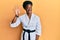 Young african american girl wearing karate kimono and black belt showing and pointing up with fingers number five while smiling