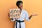 Young african american girl wearing karate kimono holding woman power banner celebrating achievement with happy smile and winner