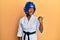 Young african american girl wearing taekwondo kimono and protection helmet pointing thumb up to the side smiling happy with open