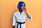 Young african american girl wearing taekwondo kimono and protection helmet shouting and screaming loud to side with hand on mouth