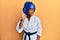 Young african american girl wearing taekwondo kimono and protection helmet smiling with hand over ear listening and hearing to