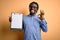 Young african american inspector man wearing glasses holding clipboard checklist doing ok sign with fingers, excellent symbol